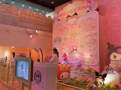 The ride as seen from the line. There is a car in the shape of My Melody
waiting for a passenger; and a large map of the route on the wall behind it. A
staff member stands behind a podium with Kuromi's Rent-a-car logo on
it.